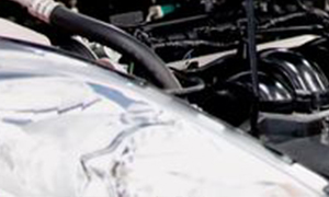 The image shows a close-up view of a vehicle s engine bay with various mechanical components visible, including a large black plastic cover over part of the engine and other metallic parts.